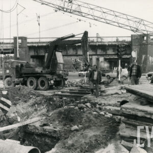 trzech mężczyzn stojących przy ciężkim sprzęcie budowlanym na tle wiaduktu kolejowego 