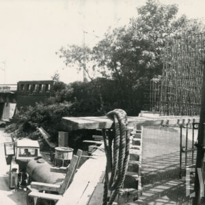 plac budowy, na którym widać stalową linę, szalunki, w głębi wiadukt kolejowy i ulica z samochodami 