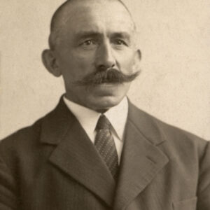 zdjęcie portretowe starszego mężczyzny z bujnym wąsem ubranego w garnitur, białą koszulę i krawat 