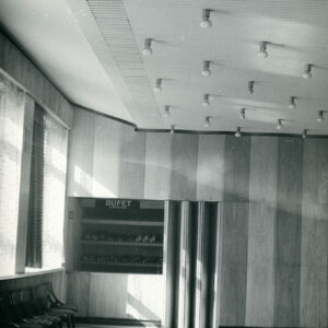 fragment dużej, jasnej sali z małym bufetem za harmonijkowymi drzwiami, na suficie sali rzędy żarówek
