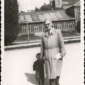 starszy mężczyzna trzyma za rękę małego chłopca, w tle szklane pawilony palmiarni