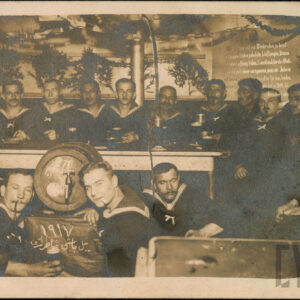 grupa mężczyzn w strojach marynarzy, pijąca piwo, większość z nich siedzi przy stole, czterech kuca przy beczce z piwem