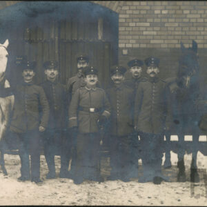 grupa mężczyzn w średnim wieku w pruskich mundurach polowych pozująca do zdjęcia w towarzystwie dwóch koni na tle ceglanego budynku