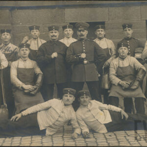 grupa młodych mężczyzn w pruskich mundurach roboczych pozująca do zdjęcia na tle ceglanego budynku, dwóch z nich leży, dwóch siedzi, pozostali stoją