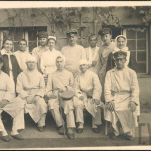 grupa hospitalizowanych mężczyzn i trzy pielęgniarki pozujący na tle budynku porośniętego bluszczem; mężczyźni noszą piżamy szpitalne, a część z nich dodatkowo czapki wojskowe