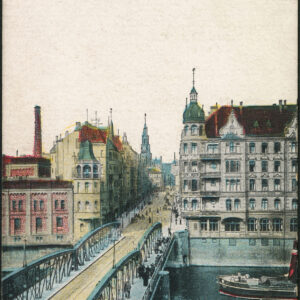 most z żelaznymi przęsłami, po nim idą ludzie, w głębi ulica, na jej narożnikach okazałe ozdobne kamienice, rzeką płynie statek