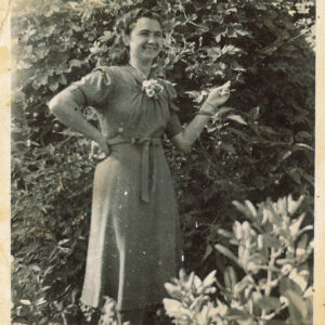 uśmiechnięta młoda kobieta w sukience z krótkim rękawem stoi na tle bujnej roślinności ogrodowej