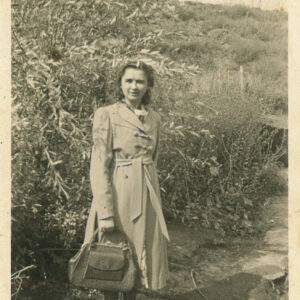 kobieta w płaszczu z torebką w ręku stoi na tle zarośli