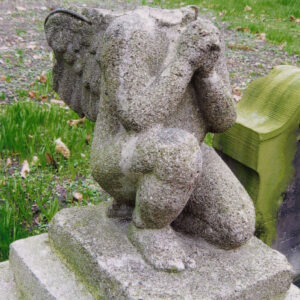 Figura anioła pozbawionego głowy z rękoma złożonymi do modlitwy umieszczona na postumencie.