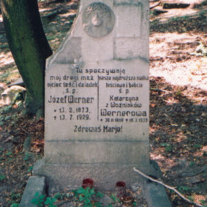 uszkodzona, pionowa płyta nagrobna z odłamanym lewym narożem, płaskorzeźbą Chrystusa i czarnymi napisami