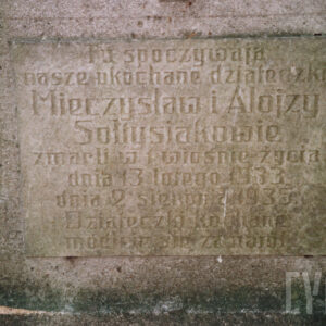 biała tablica epitafijna z wyrytymi napisami umocowana do płyty nagrobnej