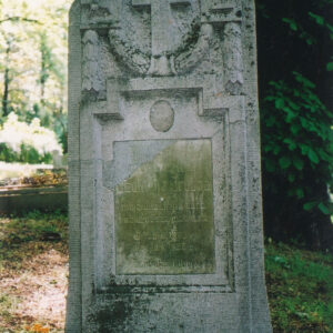 wysoka stela umieszczona na cokole, w której zwieńczeniu znajduje się krzyż łaciński, poniżej tablica epitafijna, wokół teren cmentarza