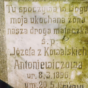 kwadratowa, biała tablica z wyrytymi napisami, umocowana do płyty nagrobnej