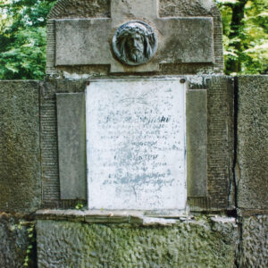 duża płyta nagrobna z krzyżem łacińskim, na którym znajduje się tondo z głową Chrystusa, poniżej biała tablica epitafijna