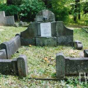 masywna płyta nagrobna z wtopionym krzyżem i białą tablicą epitafijną z wysokim, częściowo uszkodzonym obmurowaniem mogiły ziemnej, wokół teren cmentarza