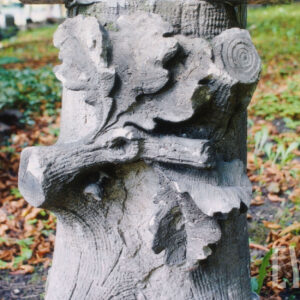 kamienny nagrobek w formie ściętego pnia drzewa, w połowie wysokości wyobrażenie ściętej gałęzi z wachlarzowato ułożonymi dębowymi liśćmi