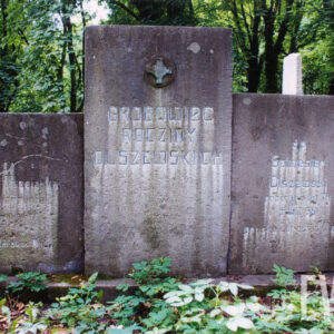 u wezgłowia ziemnej mogiły wysoka prostokątna stela, po jej bokach niższe lekko cofnięte płyty, prawa płyta przylega do kamiennego słupka sąsiedniego grobu, na każdej płycie zniszczone napisy, w partii środkowej, na górze metalowy równoramienny krzyż z kołem na skrzyżowaniu ramion, wtopiony w metalowe tondo