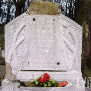 płyta przechodząca pierwotnie w wieńczący krzyż, osadzona na schodkowym postumencie, na steli tablica inskrypcyjna rozszerzająca się ku dołowi z wyrytym na niej napisem, przymocowana dwoma metalowymi nitami, po dwóch pozostały ślady, po bokach stylizowane gałązki cierniowe, postument poprzedzony donicą na kwiaty, z prawej, za mogiłą pień drzewa