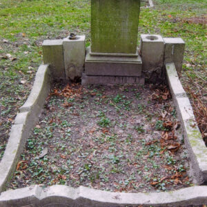 mogiła ziemna otoczona obmurowaniem o wklęsło-wypukłych krawędziach pośrodku każdego boku, u wezgłowia czworoboczny postument osadzony na niskim cokole, w zwieńczeniu profilowany, na jego szczycie cokolik pod nieistniejący krzyż, lico postumentu wypełnia ryty napis, wokół nagrobka zielona trawa