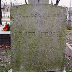 prostokątna płyta zamknięta spłaszczonym łukiem ze śladami pęknięć, na jej szczycie czworoboczna podstawa pierwotnego krzyża, na płycie wyryty napis