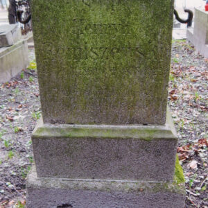 czworoboczny kamienny postument z wyrytym napisem, po bokach dwa metalowe uchwyty dawnego ogrodzenia, postument osadzony na uskokowo rozszerzającym się cokole, całość pokryta zielonym nalotem