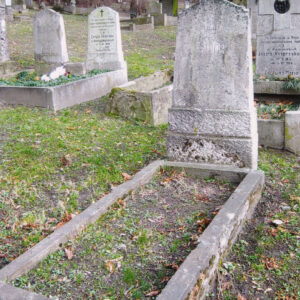 mogiła ziemna obmurowana, u wezgłowia trapezoidalna, lekko zwężająca się ku górze tablica nagrobna zwieńczona spłaszczonym z dwoma uskokami, ustawiona na wysokim, dwustopniowym cokole, w głębi murowane nagrobki