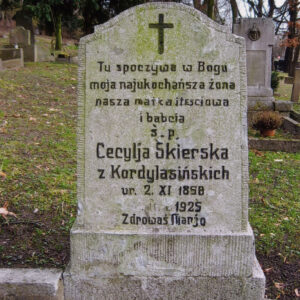 pionowo ustawiony prostokąt zamknięty spłaszczonym łukiem wklęsło-wypukłym z dwoma uskokami osadzony na wysokim dwustopniowym cokole, na tablicy ryty napis poczerniony, częściowo zatarty, na górze tablicy krzyż łaciński, w głębi kamienne nagrobki