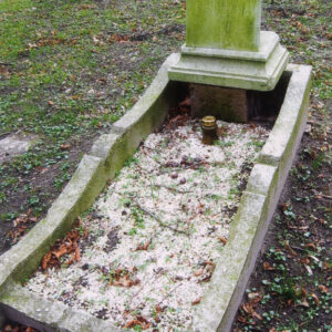 mogiła ziemna w kształcie prostokątna otoczona obmurowaniem o wklęsło-wypukłym górnym brzegu, u wezgłowia tablica inskrypcyjna przechylona ukośnie do tyłu i oparta na konsoli, górna część płyty odłamana z zielonym nalotem