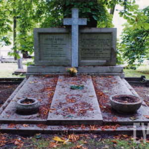 nagrobek w formie dyptyku rozdzielonego pośrodku krzyżem łacińskim o ramionach wystających ponad płyty inskrypcyjne, grób przykryty trójdzielną płytą, z których środkowa jest podwyższona, w partii nóg dwie kamienne koliste wazy, w głębi drzewa