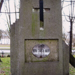 wysoka stela osadzona na prostopadłościennym cokole, złożona z pionowo ustawionej prostokątnej płyty o ściętym schodowo górnym lewym narożu, po jej bokach dwa, wąskie skrzydła obniżające się schodkowo, lewe z nich wyższe, pośrodku płyty, nad płyciną łaciński krzyż z czarnego szkła (częściowo uszkodzony), w płycinie wtórnie zamontowana blaszana, owalna tabliczka epitafijna z czarnym napisem na białym tle