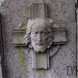 na gładkiej płycie płaskorzeźbiona głowa Chrystusa na tle krzyża