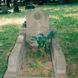 mogiła ziemna, obramowana szerokim kamiennym murkiem, w części zagłówkowej tablica zakończona łukiem (z prawej strony uszkodzona), w jej górnej części w okrągłym medalionie głowa Chrystusa w koronie cierniowej, poniżej dekoracja roślinna