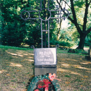 mogiła ziemna z metalowym, ażurowym krzyżem na postumencie, ramiona zakończone okręgami