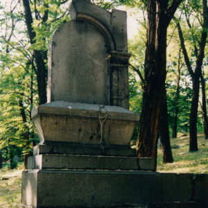 nagrobek w kształcie ołtarza osadzonego na prostokątnej, kamiennej płycie, na szczycie krzyż łaciński, w głębi drzewa