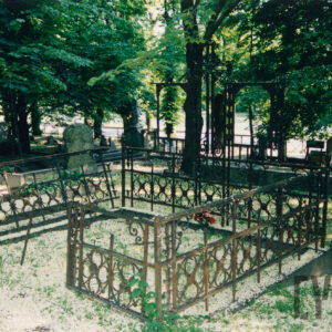 mogiła ziemna ogrodzona kutym, metalowym ogrodzeniem osadzonym na niskiej granitowej podmurówce, w części zagłówkowej pośrodku kuty żeliwny krzyż o trójlistnie zakończonych ramionach z rozetką pośrodku, po bokach dwa prostokątne obramienia tablic inskrypcyjnych (brak tablic) , w głębi kamienne nagrobki i drzewa