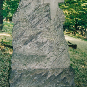 kamienna stela w formie nieregularnego kopca skalnego o chropowatej powierzchni i ukośnych nacięciach, z bryły kopca wyodrębniono krzyż łacińskich o gładkich ramionach, na steli motywy roślinne paproci ( u dołu, z lewej) i gałązki dębowej (pod krzyżem)