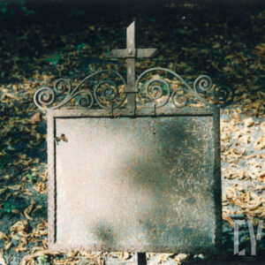 metalowa tablica z obramowaniem zakończonej pośrodku łacińskim krzyżem ujęty po bokach w kręte, fantazyjne linie, całkowicie nieczytelny napis na tablicy