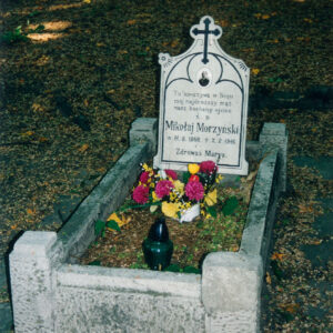 mogiła ziemna obramowana murkiem, w jego narożach czworoboczne słupki, w części zagłówkowej tablica ułożona pod lekkim skosem, na niej inskrypcja z fotografią w owalu, nad nią krzyż, całość wypełniona czarnym barwnikiem