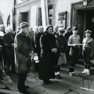 grupa ludzi, wśród nich kobieta, mężczyzna i harcerze, stoi na chodniku przed kamienicą na Starym Rynku