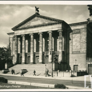 neoklasycystyczny budynek z sześciokolumnowym portykiem, zwieńczony rzeźbą konia ze skrzydłami do którego prowadzą monumentalne schody z rzeźbami po obu stronach, na pierwszym planie ulica, chodnikiem spacerują ludzie