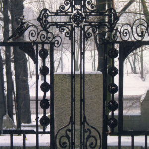 w części zagłówkowej pośrodku kuty żeliwny krzyż o trójlistnie zakończonych ramionach z rozetką pośrodku, po bokach dwa prostokątne obramienia tablic inskrypcyjnych (brak tablic) , w głębi pnie drzew; sceneria zimowa