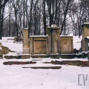 duży murowany, silnie uszkodzony nagrobek z wysokimi płycinami  i dorycką kolumną pośrodku w części zagłówkowej oraz prostopadłościennymi kolumnami w narożach, nagrobek niesymetryczny, sceneria zimowa