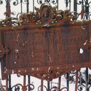 żeliwna płyta inskrypcyjna w formie prostokąta okolona liśćmi akantu i palmetkami oraz głową Chrystusa zawieszona na metalowej kracie grobowca