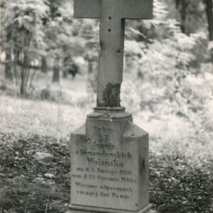 na profilowanym, zwężającym się uskokowo marmurowym cokole uszkodzony, prosty, łaciński krzyż, pod nim napis, u podstawy sygnatura, w głębi drzewa