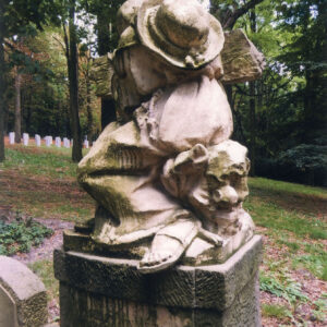 rzeźba klęczącego, starszego mężczyzny w długiej szacie, bosego w sandałach, z kapeluszem na plecach obejmującego krzyż stojący na postumencie, pod krzyżem inskrypcja