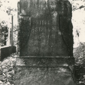 nieregularnie obrobiony blok kamienny zamknięty łukiem, umieszczony na prostopadłościennej podstawie, na bloku wypukło rzeźbiony, wychodzący lekko przed lico, gładki krzyż o belce poprzecznej przechodzącej w łuk z dolną belką rozszerzająca się, na krzyżu ryta inskrypcja