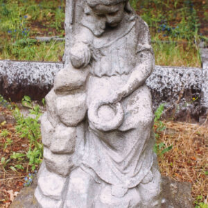 kamienny kopiec z dużych ciosów kamienia, na nich siedząca dziewczynka w długiej sukni o dużym dekolcie, głowa lekko przechylona na prawe ramię, prawa ręka odłamana na wysokości łokcia, lewa opuszczona na udo, w niej wieniec