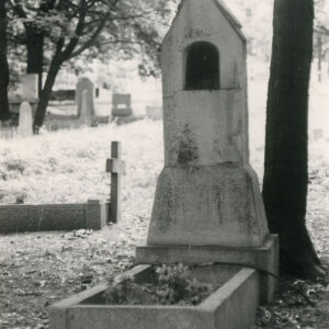 mogiła ziemna obramowana wąskimi ściankami, w partii zagłówkowej murowana kapliczka stylizowana na przydrożną, zamknięta trójkątnym szczytem nakrytym dwuspadowym daszkiem pokrytym dachówką, na jego szczycie metalowy krzyż, w górnej części kapliczki płytka nisza, z prawej pień drzewa