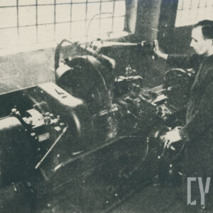 mężczyzna w średnim wieku w stroju roboczym, stojący przy urządzeniu mechanicznym ustawionym w hali z oknami