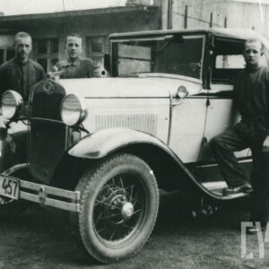 trzech młodych mężczyzn w strojach roboczych, pozujących do fotografii przy eleganckim samochodzie